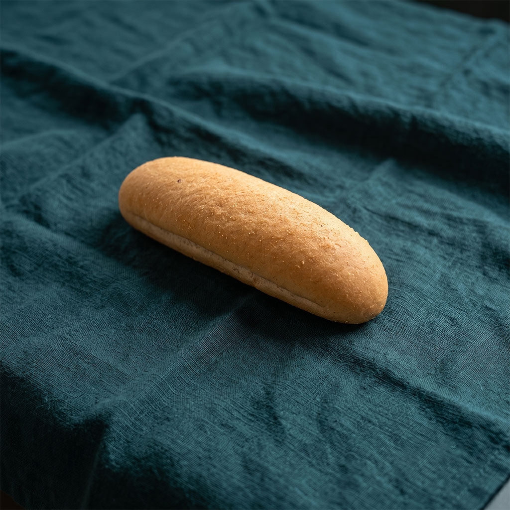 Hosszúkás, lágy textúrájú hot-dog kifli sötétzöld alapon.