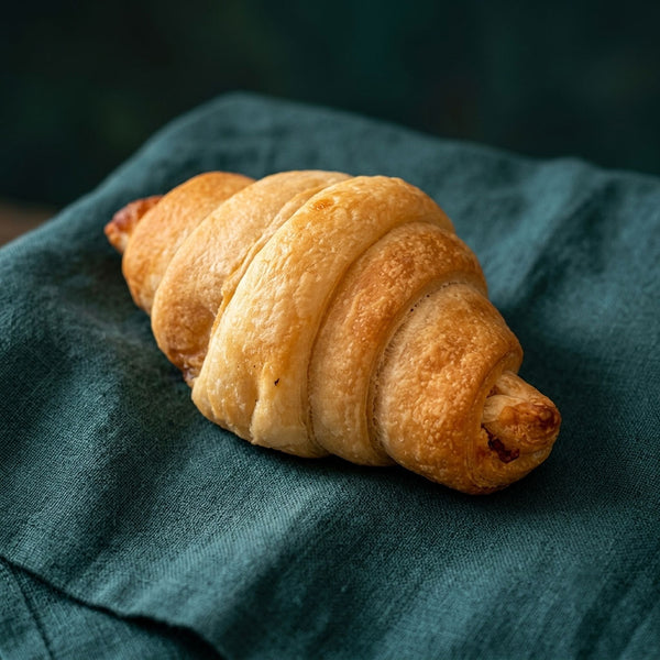 Ropogós, réteges leveles tésztájú baconös croissant zöld terítőn.