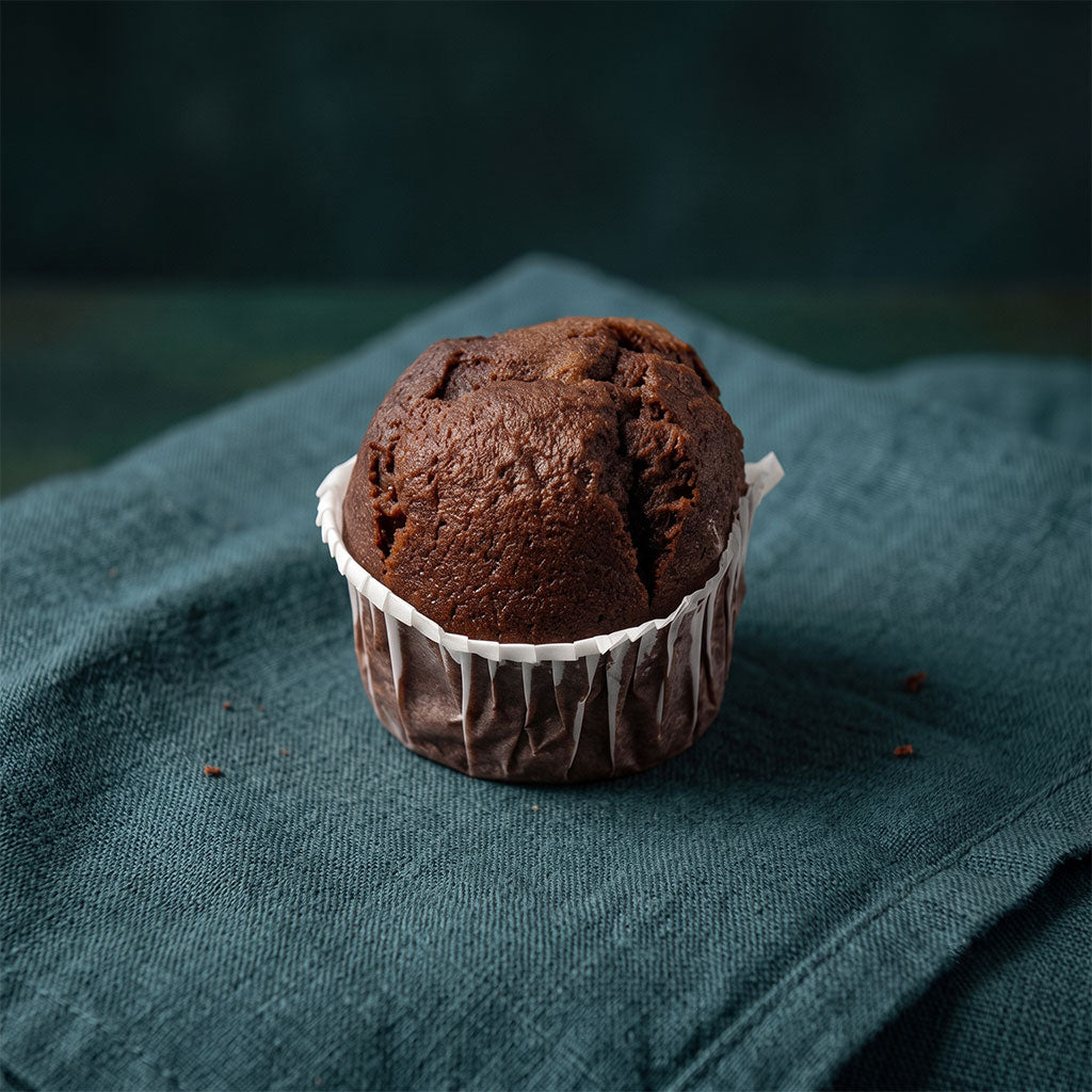 Puha csokoládés muffin muffinpapírba csomagolva sötétzöld szalvétán.