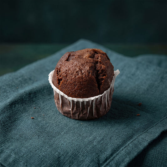 Puha csokoládés muffin muffinpapírba csomagolva sötétzöld szalvétán.
