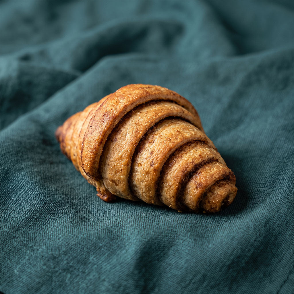 Sűrűn rétegzett, aranybarna fahéjas croissant sötétzöld textílián.