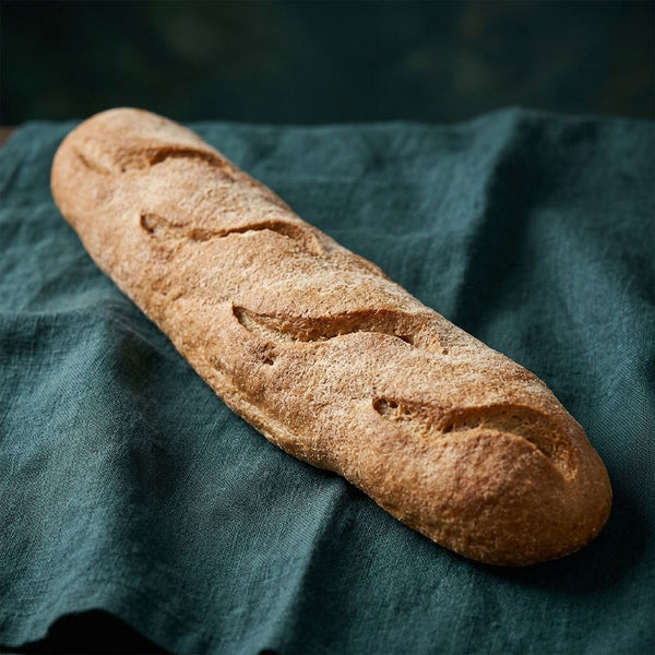 Hosszú, vékony francia bagett ropogós kéreggel és bevágásokkal, sötétzöld terítőn.