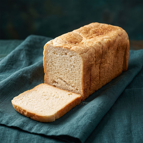 Szeletelt, puha belsejű, aranybarna héjú szögletes toastkenyér, mellette egy levágott szelettel.
