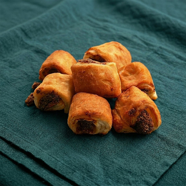 Kisebb, falatnyi méretű, ropogós húsos táskák halomban elhelyezve egy sötétzöld terítőn.