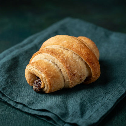 Krémes csokoládétöltelékes, aranybarna croissant sötétzöld terítőn.