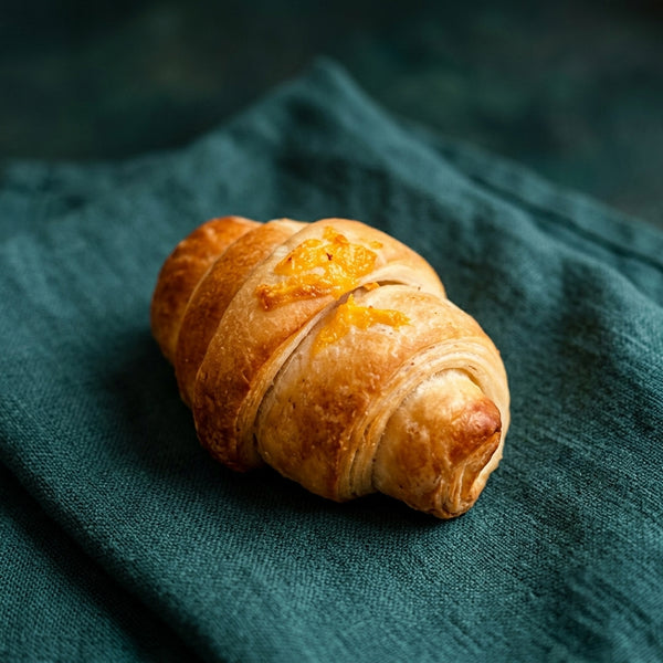 Aranyló színű, sajtos töltelékes croissant darabka reszelt sajttal megszórva.
