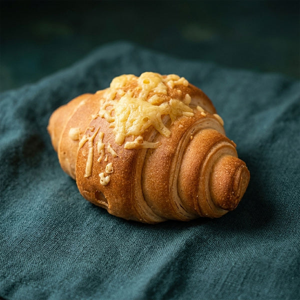 Hagyományos formájú, ropogós sajtos croissant tetején aranyszínű, olvadt sajtréteggel.