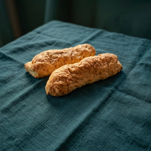 Két darab, rusztikus formájú sajtos stangli sötétzöld terítőn.